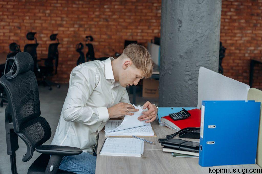 a-man-scanning-a-book-8297361 Business professional deeply focused on analyzing paperwork in a modern office setting.